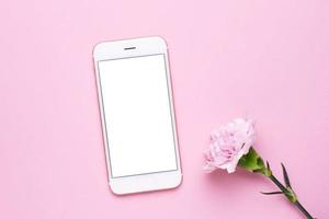 Mobile phone mock up and pink flower on pink pastel table in flat lay style. Woman working desk. photo