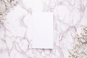 Empty card with white flowers on marble table top view and flat lay style. photo