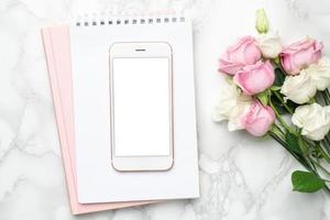 Mobile phone with pink and white roses flowers on marble background.Minimalistic composition for the holidays,valentines day and womens day. photo