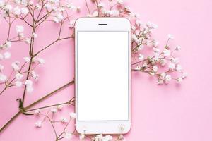 Mobile phone mock up and white flowers on pink pastel table in flat lay style. Woman working desk. photo