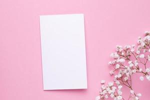 Presente la tarjeta con flores blancas en la vista superior de la mesa rosa pastel y estilo plano. color de moda de verano. foto