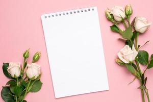 Beautiful white roses flower and notebook on pink background photo