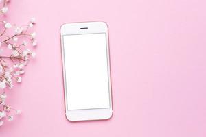 Mobile phone mock up and white flowers on pink pastel table top view in flat lay style. Woman working desk. photo