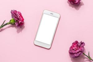 Mobile phone mock up and pink flowers on pink pastel table top view in flat lay style. Woman working desk.Spring colour photo