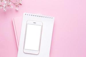 maqueta de teléfono móvil y flores blancas en la vista superior de la mesa rosa pastel en estilo plano. escritorio de trabajo de mujer. foto