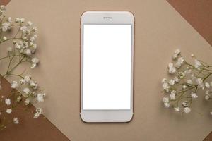 Mobile phone with white screen and dry flower branch and stone on a light brown background. Trend, minimal concept with copyspace photo