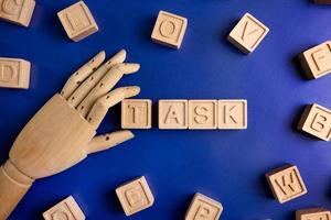 TASK the word on wooden cubes with wooden hand on blue background . Business and finance concept photo