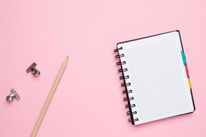 Notebook in a cage with pencil on a pink background photo