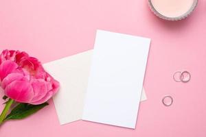 tarjeta de felicitación con una hermosa flor de peonía y accesorios de mujer sobre un fondo rosa pastel. color de moda de verano. foto