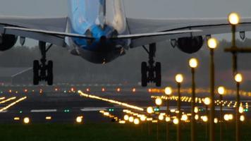 The wide bodied aircraft lands on the illuminated runway in the early morning video