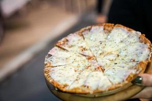 La pizza de jamón con queso se rellena con orégano en la mano de una mujer. Evento de pista de comida en bangkok, thialand. foto