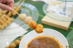 Young female's hand holding pork meat ball stick with Thai sauce style on it. photo