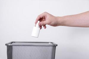A hand throws a plastic tube into the trash against a gray background. photo