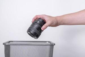 Hand throws photo lens in the trash on a gray background.