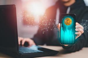 Smartphone with Bitcoin chart on-screen among piles of Bitcoin concept. businessman touch on mobile app screen with big BUY and SELL buttons on the stock market, Cryptocurrency and finance. photo