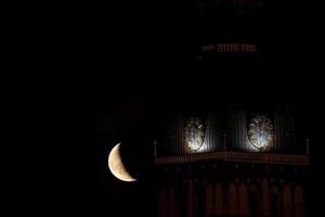 hermoso cuarto de luna sobre el casco antiguo de riga detrás de las cúpulas del reloj de la catedral. foto