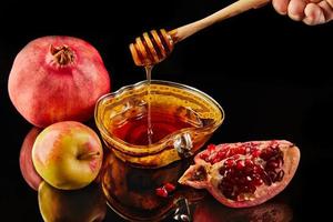 Rosh hashanah - jewish new year holiday concept. Apple-shaped bowl with honey, apples, pomegranates, shofar on black background with reflection photo