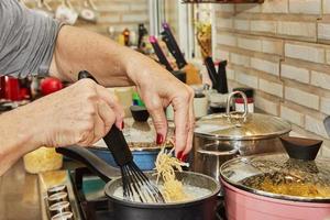 el chef echa queso rallado en una olla de salsa bechamel, que se está cocinando en una estufa de gas foto