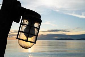 Silhouette of Retro streetlight, bulb hanging on wooden electric pole. Vintage pillar with lamp. Clear empty blue sky background, copy space. Old Lantern photo