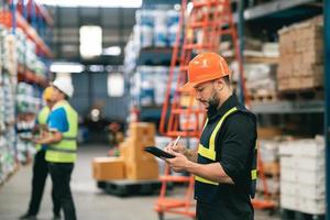 Professional manager man employee using tablet check stock working at warehouse. Worker wearing high visibility clothing and a hard hat, helmet and checking and count up goods or boxes for delivery. photo