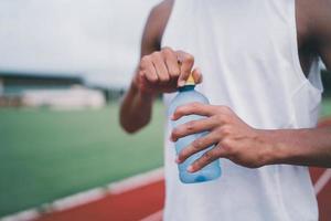 Close up of hand sport man hold bottle water runner tired and thirsty after running workout drinking water. Sport man concept photo