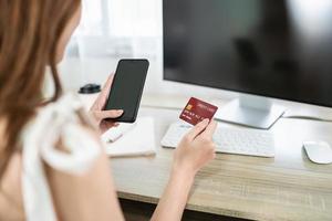 Woman holding credit card and using mobile to shopping online. asian woman working at home. Online shopping, e-commerce, internet banking, spending money, working from home concept. photo