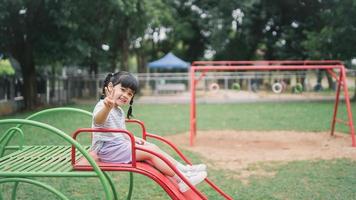 Cute asian girl play on school or kindergarten yard or playground. Healthy summer activity for children. Little asian girl climbing outdoors at playground. Child playing on outdoor playground. photo
