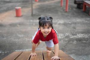 linda chica asiática juega en la escuela o en el jardín de infantes o en el patio de recreo. Actividad de verano saludable para niños. niña asiática escalando al aire libre en el patio de recreo. niño jugando en el patio de recreo al aire libre. foto