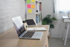 Close up view of worktable with laptop or computer, tablet, notebook, pen and post-it note in home office room. Work at home place in the living room concept. photo