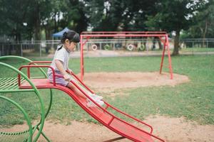 linda chica asiática juega en la escuela o en el jardín de infantes o en el patio de recreo. Actividad de verano saludable para niños. niña asiática escalando al aire libre en el patio de recreo. niño jugando en el patio de recreo al aire libre. foto