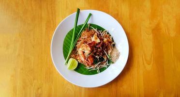 Top view of stir fried with rice noodle, river prawn or shrimp, bean sprout, sliced chives and lime on banana leaf with copy space. Flat lay of Famous food in Thailand call Pad Thai. photo