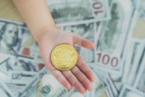 Close up of hand baby holding gold bitcoin crypto currency blockchain on dollar bill background on table. Crypto currency blockchain Saving investment wealth concept. photo