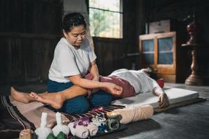 masaje y spa tratamiento relajante del síndrome de la oficina estilo tradicional de masaje tailandés. asain, masajista femenina senior que hace masajes, trata la mano, el dolor de espalda, el dolor de brazos, los pies y el estrés de las ancianas cansadas. foto