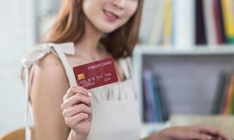 Woman holding showing credit card to shopping online. asian woman working at home. Online shopping, e-commerce, internet banking, spending money, working from home concept.