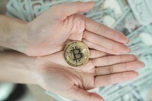 Close up of hand woman holding gold bitcoin crypto currency blockchain on dollar bill background on table. Crypto currency blockchain Saving investment wealth concept. photo