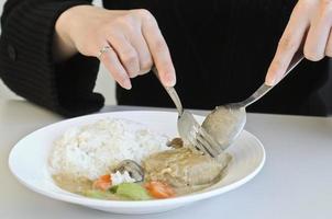 una dama comiendo arroz al curry con cuchara y tenedor foto