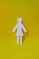 Silhouette of a woman in dress of white paper, cut by hand. In the center of vertical photo on yellow background