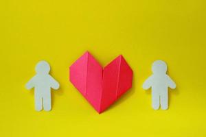 dos siluetas de personas están talladas en papel blanco con un corazón de origami entre ellas sobre un fondo amarillo. el concepto de amor, relaciones, familia foto