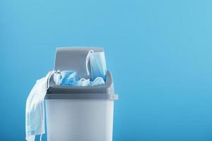 Waste bin full of used protective masks on a light blue background with free space. photo