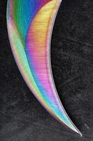 The curved sharp blade of the Kerambit Dagger is a gradient rainbow color on a dark background. photo