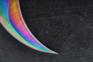 The curved sharp blade of the Kerambit Dagger is a gradient rainbow color on a dark background. photo