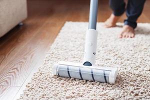 A cordless vacuum cleaner cleans the carpet in the living room with the bottom of the legs. photo