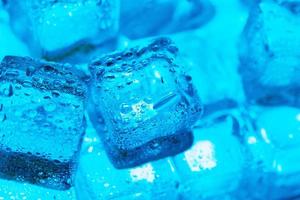 cubos de hielo con gotas de agua esparcidas sobre un fondo azul, vista superior. foto