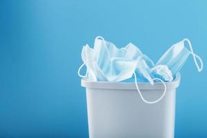 Waste bin full of used protective masks on a light blue background with free space. photo