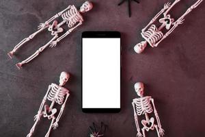 Skeletons around a smartphone with a white display on a dark background. photo