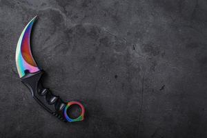 Kerambit dagger with a rainbow-colored blade on a dark textured background. photo