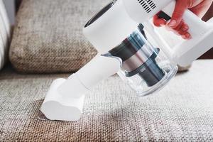 A man's hand holds a modern wireless vacuum cleaner for cleaning the sofa in the house. photo