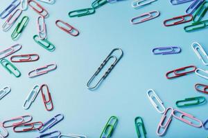 A large paper clip surrounded by small colored paper clips on a blue background photo