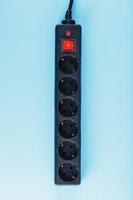 A black surge protector with portable sockets and a red button on a blue background. photo