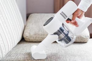 A person uses a white cordless vacuum cleaner to clean the sofa in the living room. photo